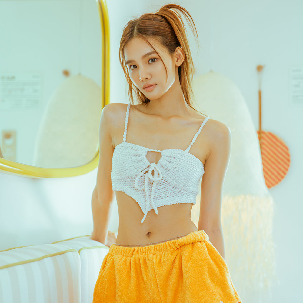 Woman wearing a white crochet top and yellow pants in a bright room.